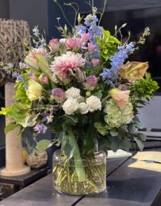 Wilder, natürlich gebundener Blumenstrauß in leuchtenden , Rosa-, creme und hellblau Tönen mit vielfältigen Wiesenblumen, ergänzt durch filigrane Gräser und frisches Grün.