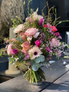 Wilder, natürlich gebundener Blumenstrauß in leuchtenden , Rosa-, creme und pinktönen mit vielfältigen Wiesenblumen, ergänzt durch filigrane Gräser und frisches Grün.