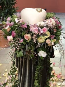 Urne in Herzform liegt in einem locker gesteckten Urnekranz aus hellrosa, pastell Blumen
