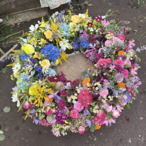 Rundgesteckter Trauerkranz aus verschiedenen bunten Blumen der Saison als Farbverlauf angeordnet