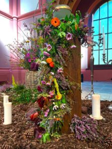 Eine bunte Blumengirlande hängt von einer Säule auf der eine Urne steht