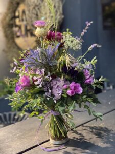 Wilder, natürlich gebundener Blumenstrauß in leuchtenden , Lila, Violett und pinktönen mit vielfältigen Wiesenblumen, ergänzt durch filigrane Gräser und frisches Grün.