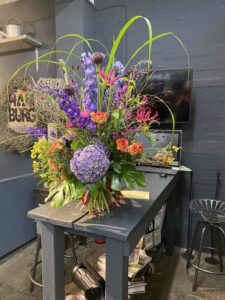 Wilder, natürlich gebundener Blumenstrauß in leuchtenden , Rosa-, orange und lilaönen mit vielfältigen Wiesenblumen, ergänzt durch filigrane Gräser und frisches Grün.