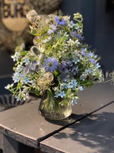 rund gebundener Blumenstrauß in hellblau, creme mit vielfältigen Wiesenblumen, ergänzt durch filigrane Gräser und frisches Grün.