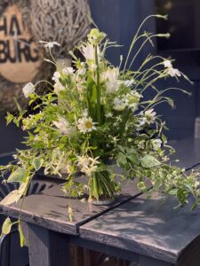Wilder, natürlich gebundener Blumenstrauß in weiß aus Wiesenblumen, ergänzt durch filigrane Gräser und frisches Grün.