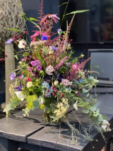 Wilder, natürlich gebundener Blumenstrauß mit vielfältigen Wiesenblumen, ergänzt durch filigrane Gräser und frisches Grün.
