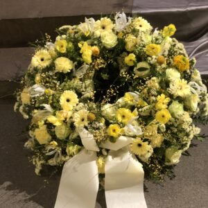 Rundgesteckter Trauerkranz aus verschiedenen bhell gelben Blumen der Saison