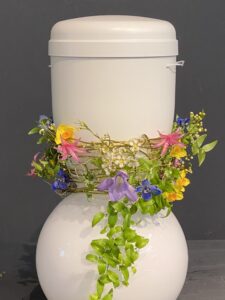 Der Fuß der Urne istmi einer zarte Girlande aus bunten kleinen Blüten umwickelt
