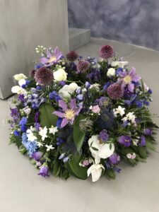Rundgesteckter Trauerkranz aus verschiedenen violett/ weißen Blumen der Saison