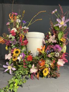 eine Urne steht in einem Bogen aus bunten, sommerlichen Blumen