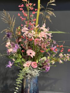 Wilder, natürlich gebundener Blumenstrauß in zarten, Rosa-, creme und lilaönen mit vielfältigen Wiesenblumen, ergänzt durch filigrane Gräser und frisches Grün.