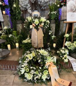 Urnekranz aus weißen Lilien, ein rundgesteckter Kranz liegt davor
