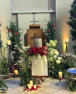 eine Urne steht in einem Urnenkranz aus roten Rosen mit Trauerschleifen
