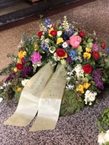 dekorativer Trauerkranz aus bunten Wiesenblumen, mit Trauerschleife